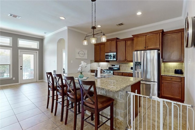 kitchen with pendant lighting, a center island with sink, a kitchen breakfast bar, light tile patterned floors, and appliances with stainless steel finishes