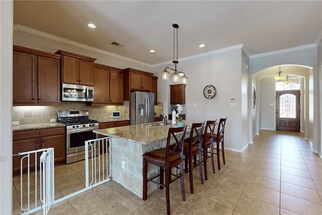 kitchen featuring light stone countertops, hanging light fixtures, a kitchen breakfast bar, a kitchen island with sink, and appliances with stainless steel finishes