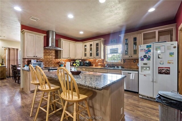 kitchen with white fridge with ice dispenser, a center island, stainless steel dishwasher, and wall chimney range hood