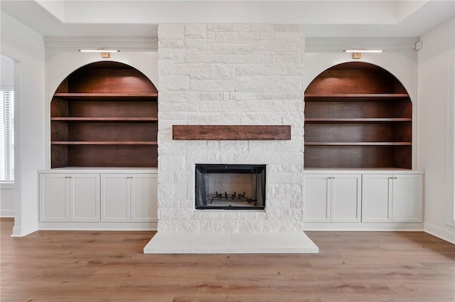 unfurnished living room with light wood-type flooring, built in features, and a fireplace