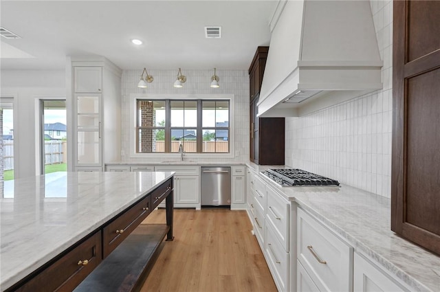 kitchen featuring white cabinets, appliances with stainless steel finishes, premium range hood, and light hardwood / wood-style flooring