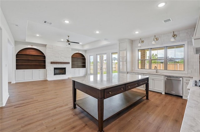 kitchen featuring light wood-type flooring, a fireplace, built in features, dishwasher, and white cabinetry