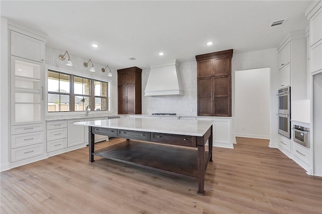 kitchen featuring light hardwood / wood-style flooring, premium range hood, backsplash, a kitchen island, and appliances with stainless steel finishes