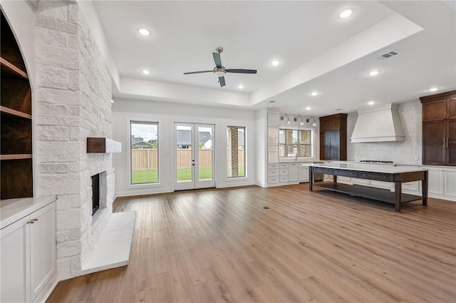 unfurnished living room featuring light hardwood / wood-style floors, a raised ceiling, ceiling fan, and a stone fireplace