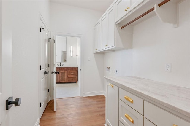 interior space with cabinets, hookup for a washing machine, hookup for an electric dryer, sink, and light hardwood / wood-style floors