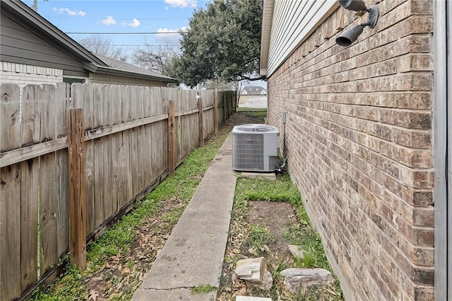 view of property exterior featuring brick siding, fence, and central AC unit