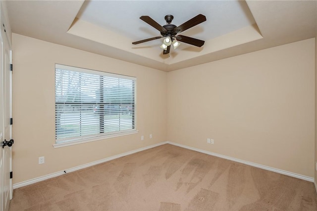 unfurnished room with a ceiling fan, a raised ceiling, light carpet, and baseboards