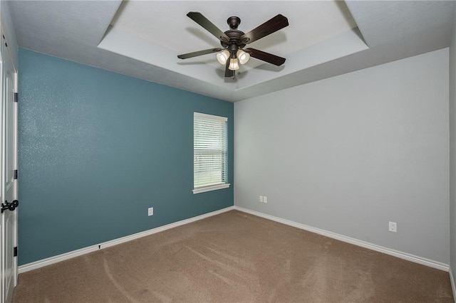 carpeted empty room with a tray ceiling, ceiling fan, and baseboards