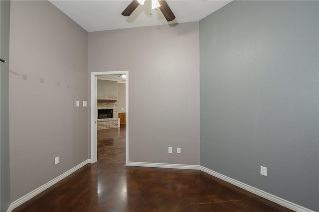 unfurnished room with concrete floors, a brick fireplace, ceiling fan, and baseboards