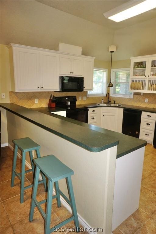 kitchen featuring decorative light fixtures, a kitchen bar, decorative backsplash, white cabinets, and black appliances