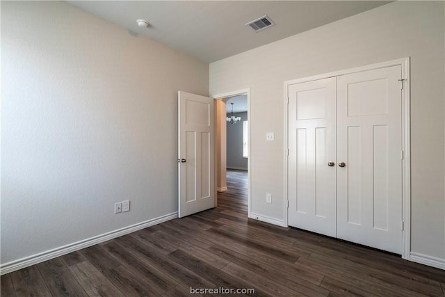 unfurnished bedroom with an inviting chandelier, dark hardwood / wood-style flooring, and a closet