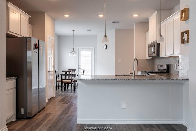 kitchen featuring dark wood-type flooring, white cabinets, appliances with stainless steel finishes, decorative light fixtures, and kitchen peninsula