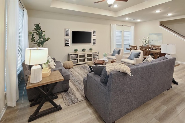 living room featuring a raised ceiling, ceiling fan, and light wood-type flooring