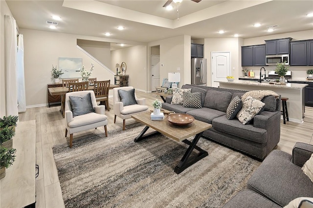 living room featuring sink, a raised ceiling, ceiling fan, and light wood-type flooring