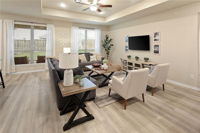 living room featuring a tray ceiling, light hardwood / wood-style flooring, and ceiling fan