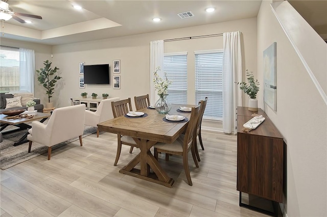 dining room with a raised ceiling, ceiling fan, and light hardwood / wood-style floors