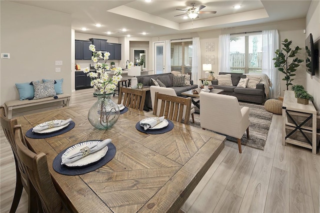 dining space with a tray ceiling, light hardwood / wood-style floors, and ceiling fan