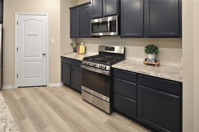 kitchen featuring tasteful backsplash, light stone countertops, stainless steel appliances, and light wood-type flooring