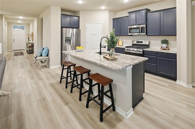 kitchen with appliances with stainless steel finishes, a breakfast bar, sink, light stone countertops, and a center island with sink