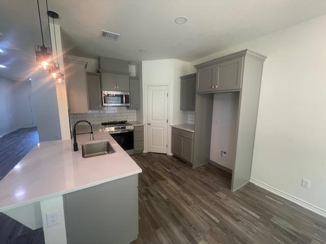 2303 White Wing Dr, Navasota, TX 77868 - kitchen with appliances with stainless steel finishes, gray cabinetry, a sink, a peninsula, and dark wood finished floors