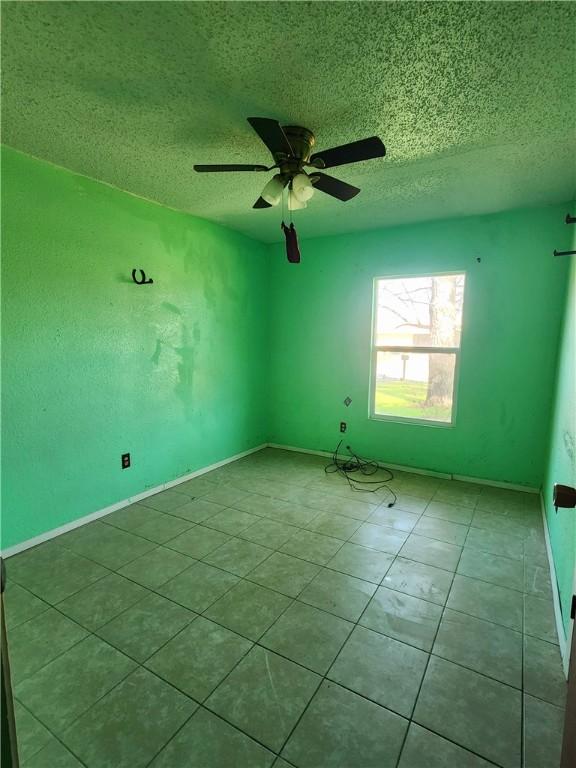 empty room featuring ceiling fan, light tile patterned floors, and a textured ceiling