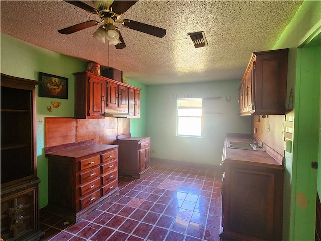 kitchen with ceiling fan, sink, a textured ceiling, and dark tile patterned floors