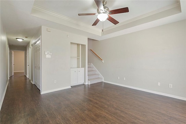 empty room with built in shelves, dark hardwood / wood-style floors, ceiling fan, and a tray ceiling