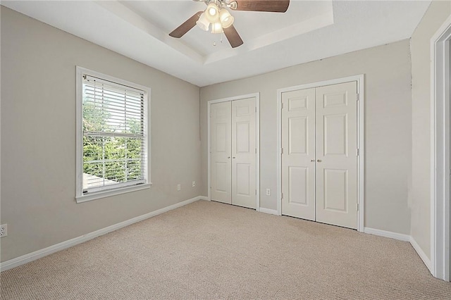 unfurnished bedroom with a tray ceiling, multiple closets, ceiling fan, and light carpet