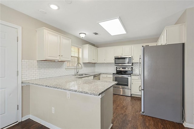 kitchen featuring white cabinets, sink, appliances with stainless steel finishes, light stone counters, and kitchen peninsula