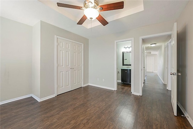 unfurnished bedroom with dark hardwood / wood-style flooring, ensuite bathroom, a raised ceiling, ceiling fan, and a closet