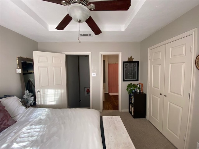 carpeted bedroom with a closet, a raised ceiling, and ceiling fan