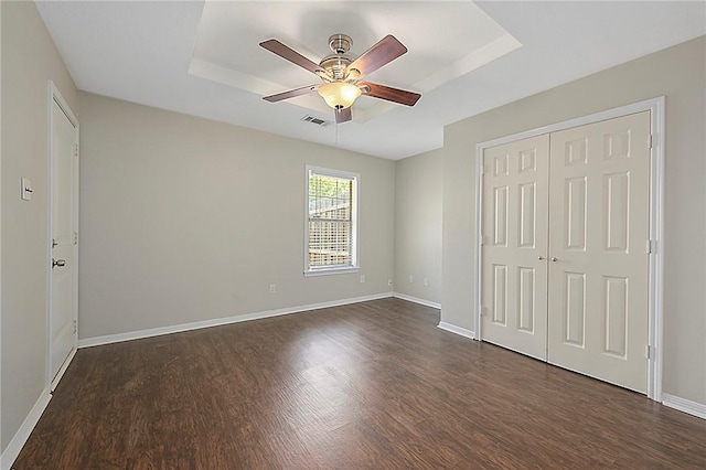 unfurnished bedroom featuring ceiling fan, a closet, dark hardwood / wood-style flooring, and a tray ceiling