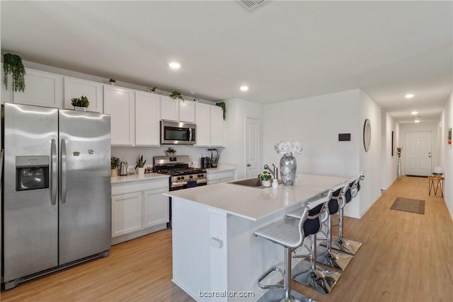 kitchen featuring a breakfast bar, stainless steel appliances, sink, white cabinets, and light hardwood / wood-style floors