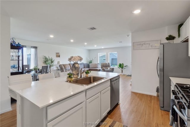 kitchen with a kitchen island with sink, white cabinets, sink, light wood-type flooring, and appliances with stainless steel finishes