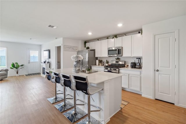 kitchen with white cabinets, a kitchen breakfast bar, a center island with sink, and stainless steel appliances