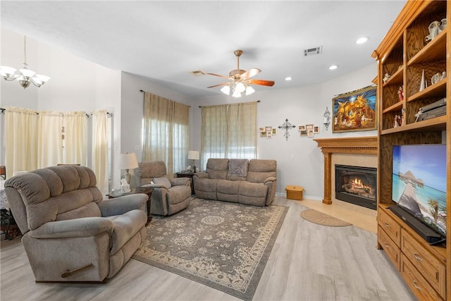 living room featuring visible vents, light wood-style flooring, a fireplace, and ceiling fan with notable chandelier