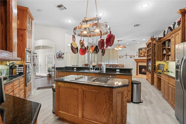 kitchen featuring visible vents, a sink, a lit fireplace, stainless steel appliances, and a center island