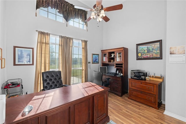 home office featuring light wood-type flooring, baseboards, a towering ceiling, and a ceiling fan