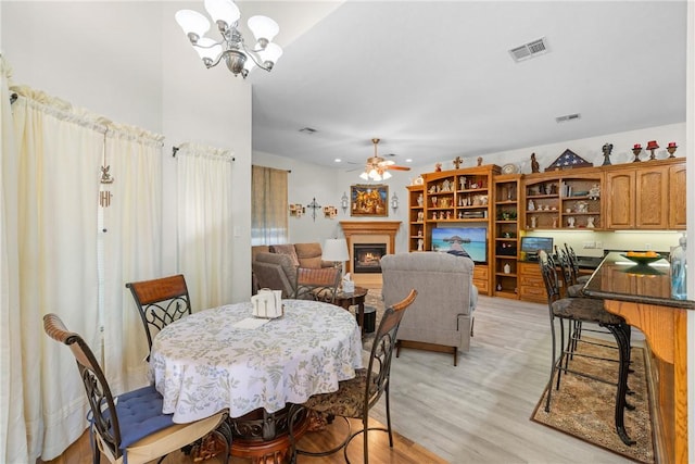 dining area with light wood finished floors, visible vents, ceiling fan with notable chandelier, and a lit fireplace