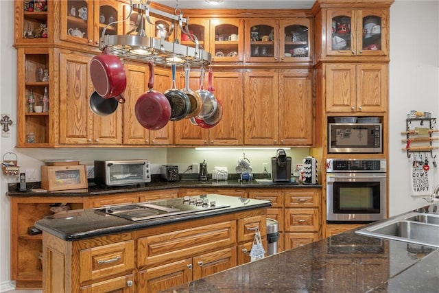 kitchen with glass insert cabinets, a toaster, appliances with stainless steel finishes, brown cabinetry, and a sink