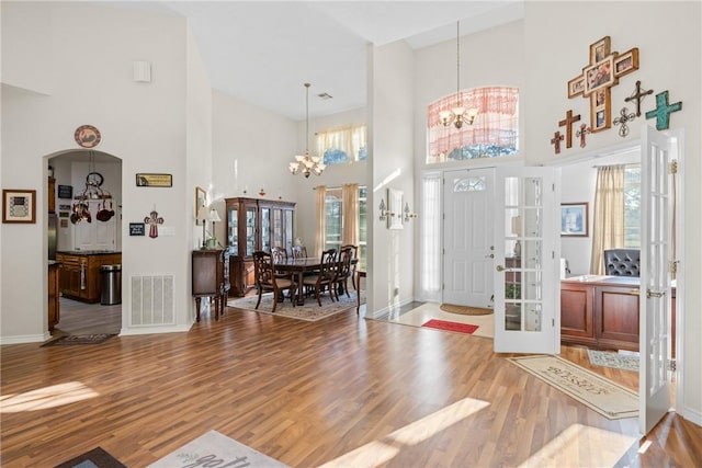 foyer entrance featuring visible vents, baseboards, wood finished floors, a towering ceiling, and an inviting chandelier