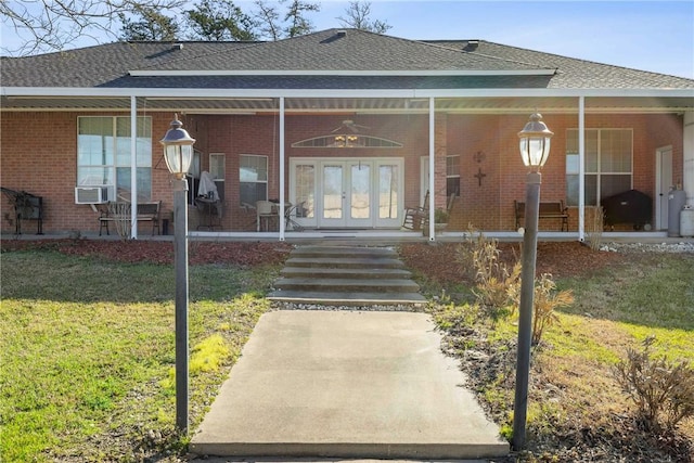 rear view of property featuring a porch, french doors, brick siding, and a lawn