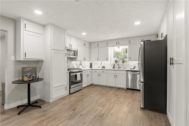 kitchen featuring sink, stainless steel appliances, a textured ceiling, white cabinets, and light wood-type flooring