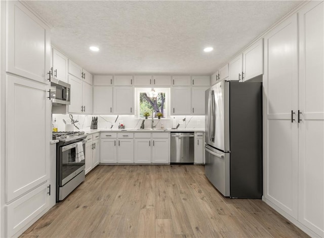 kitchen featuring sink, light wood-type flooring, a textured ceiling, appliances with stainless steel finishes, and white cabinetry