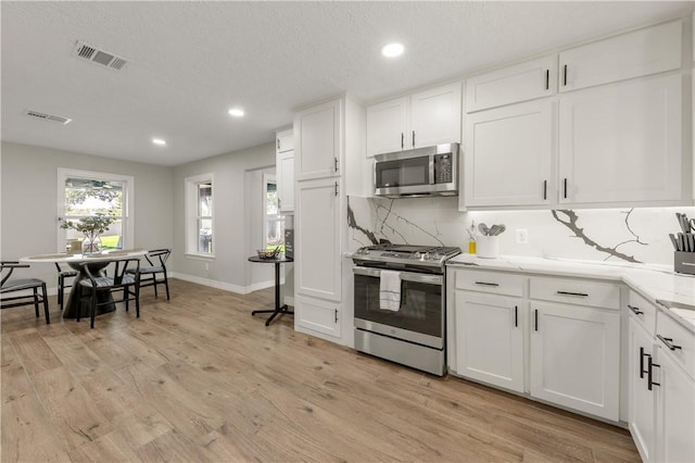 kitchen featuring tasteful backsplash, white cabinetry, light hardwood / wood-style flooring, and stainless steel appliances