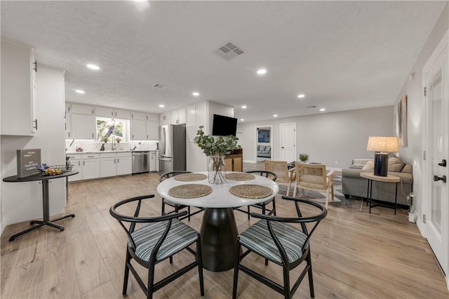 dining room with a textured ceiling, sink, and light hardwood / wood-style flooring