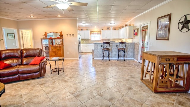 living room featuring ceiling fan, ornamental molding, a drop ceiling, and light tile patterned floors