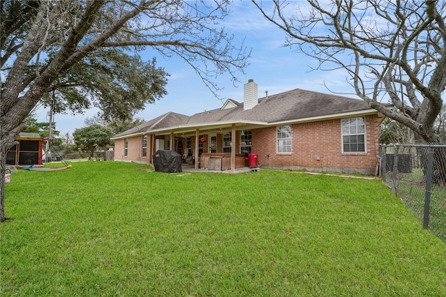 rear view of property featuring a patio, a fenced backyard, a yard, brick siding, and a chimney