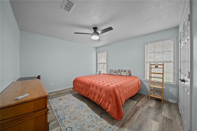 bedroom with wood finished floors, visible vents, baseboards, ceiling fan, and a textured ceiling