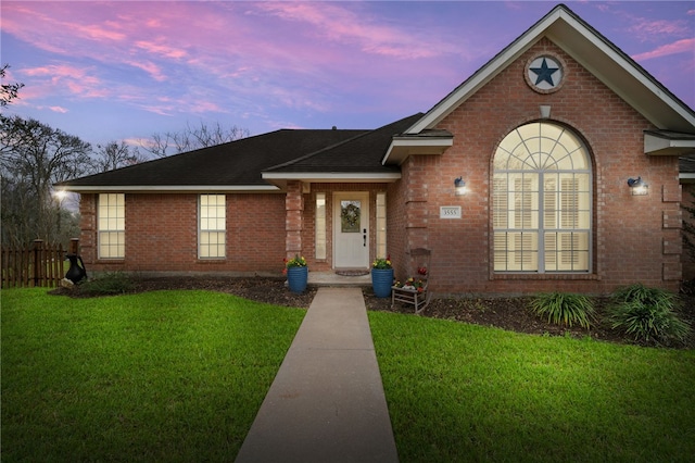 view of front of house with fence, a lawn, brick siding, and a shingled roof